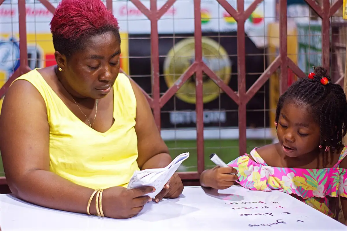 Parent sitting beside a child and helping with homework at a table